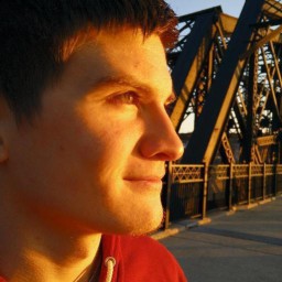 Picture of Zac Littleberry. Headshot standing on a bridge, the sun on their face. No eye contact.